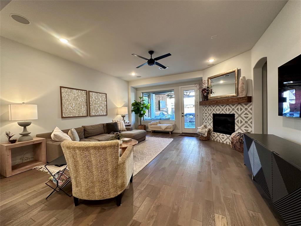 Open-concept living space featuring wood-finish flooring, recessed lighting, ceiling fan, and a fireplace with decorative tile surround and natural wood mantel