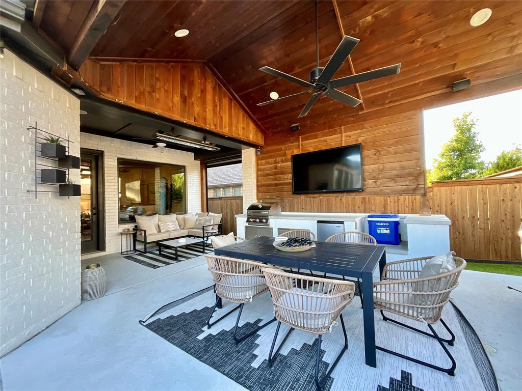 Covered patio featuring a vaulted wood-plank ceiling, recessed lighting, ceiling fan, white brick exterior walls, and a built-in outdoor kitchen with a stone countertop