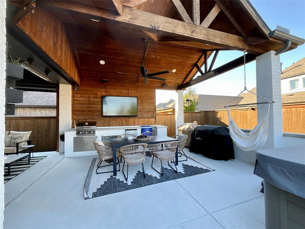 Covered patio featuring a vaulted wood-plank ceiling with exposed timber trusses, white brick support pillars, built-in stainless steel outdoor kitchen, and concrete flooring
