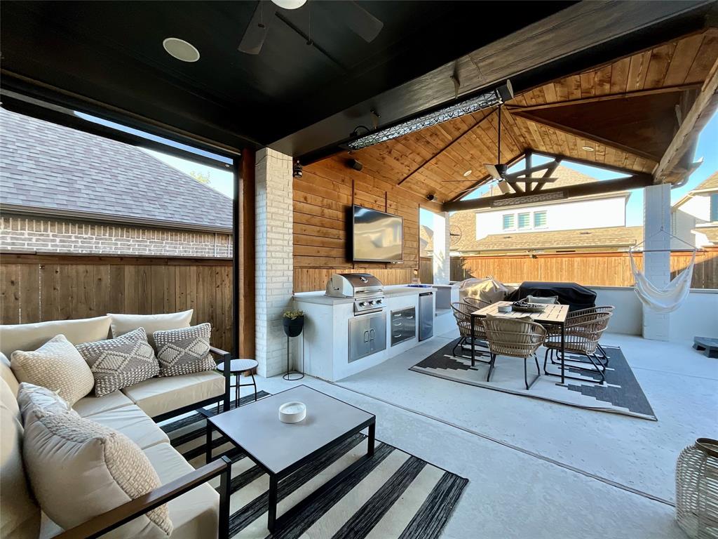 Covered patio featuring a vaulted wood-paneled ceiling, integrated outdoor kitchen with stainless steel appliances, brick-accented wall, and recessed lighting