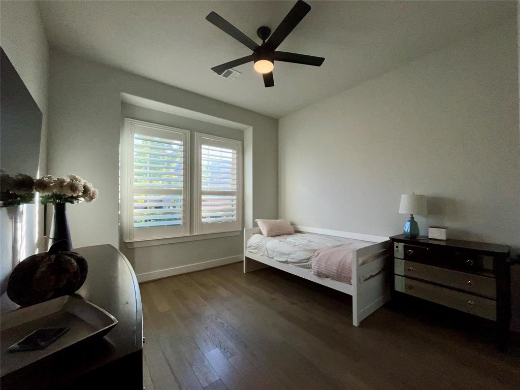 Wood-finish flooring, dual windows with plantation shutters, and a matte black ceiling fan with integrated lighting