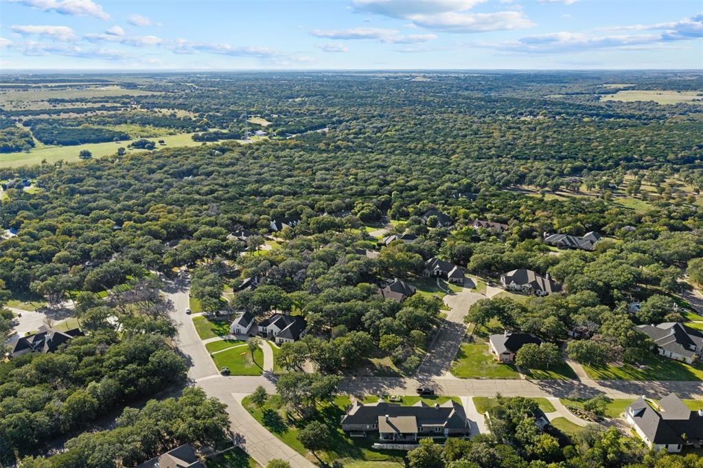Aerial perspective featuring a residential setting with paved roadways, concrete sidewalks, multi-gabled rooflines, and mature woodland canopy