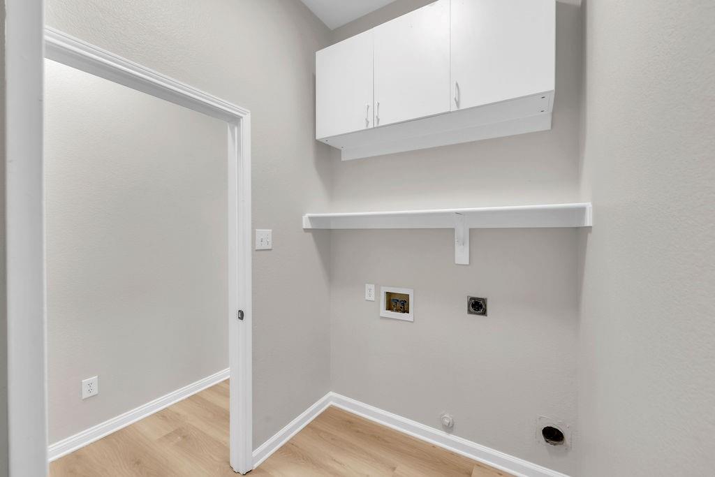 Utility area featuring wood-finish flooring, white wall-mounted cabinetry, a fixed open shelf, and dedicated water and electrical hookups