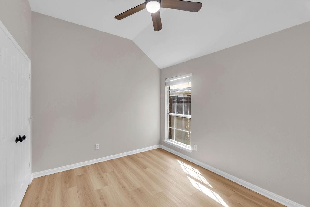Vaulted ceiling room featuring light-tone wood-finish flooring, a ceiling fan with integrated lighting, and a double-door closet