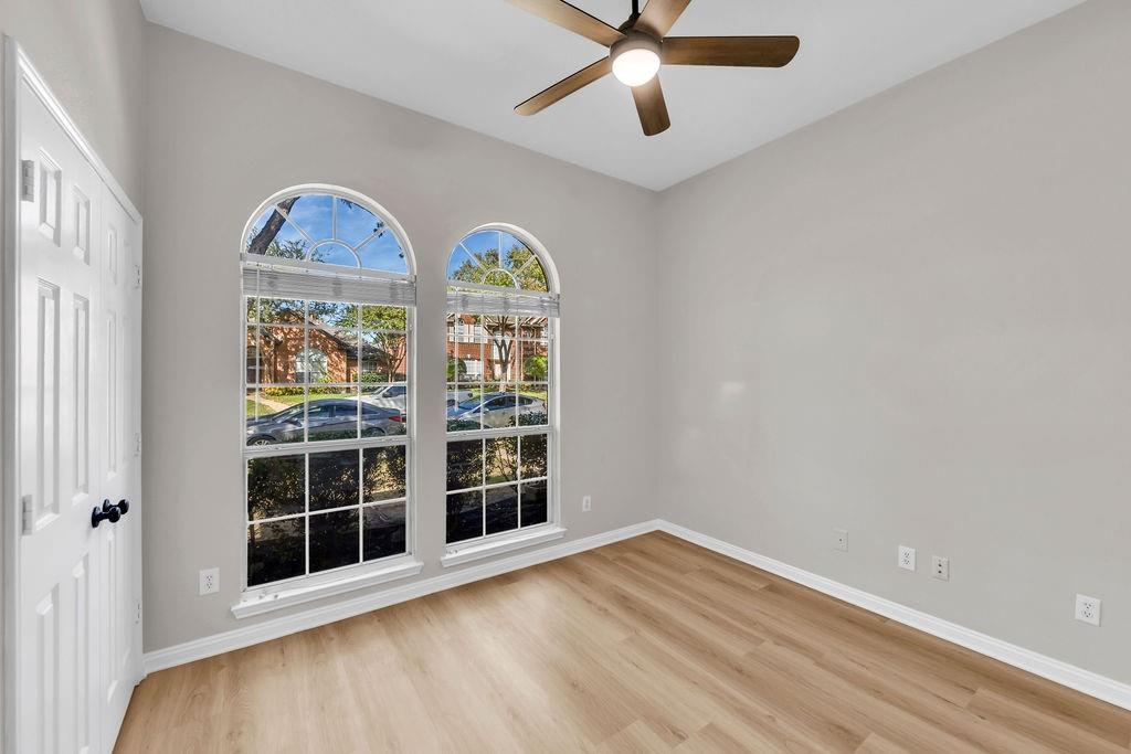 Room featuring wood-finish flooring, dual arched windows with muntins, and a ceiling-mounted light fixture with fan
