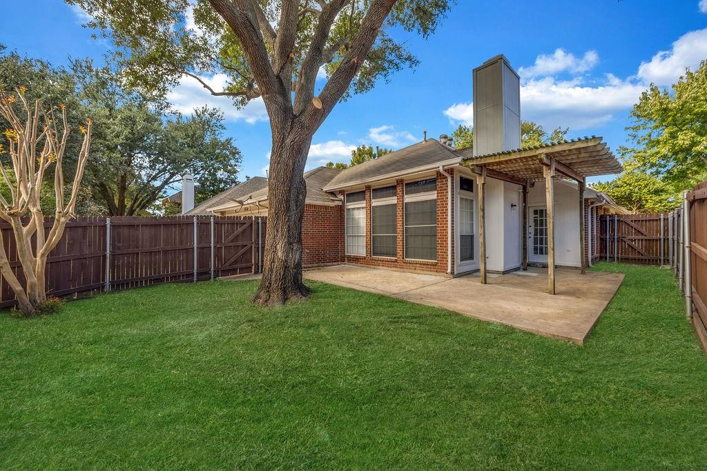 Backyard featuring a concrete patio, wood pergola, red brick exterior, chimney, and wooden privacy fencing