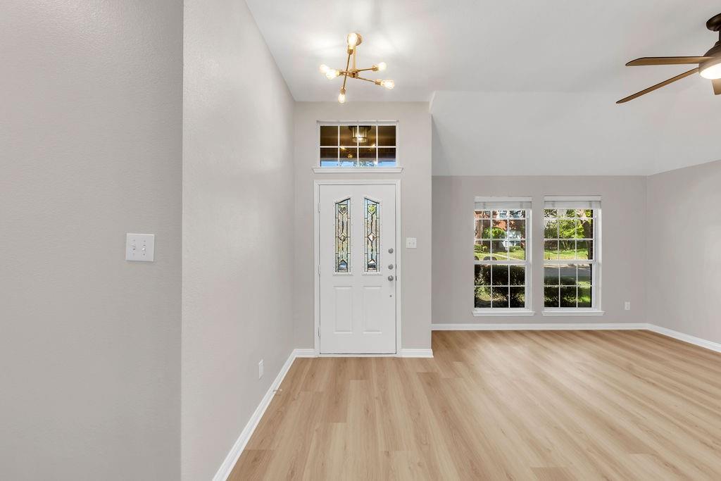 Entryway featuring wood-finish flooring, vaulted ceilings, multi-pane windows, a decorative glass-panel front door with a transom window, and a contemporary multi-arm light fixture