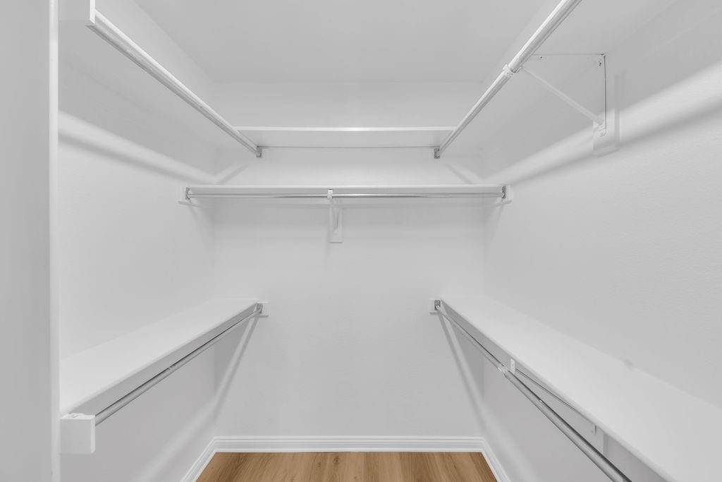 Walk-in closet featuring multi-level white shelving and integrated metal hanging rods over wood-finish flooring