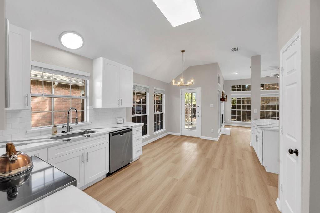 Kitchen featuring white cabinetry, wood-finish flooring, vaulted ceilings with recessed lighting, subway tile backsplash, and stainless steel appliances