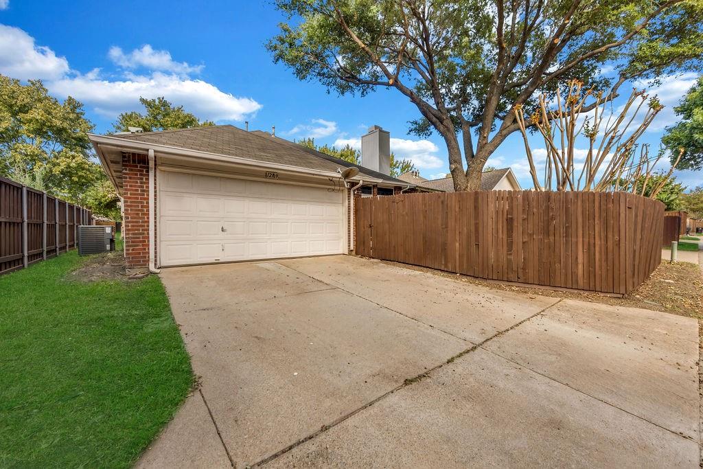Attached two-car garage with brick siding, concrete driveway, and wooden privacy fencing