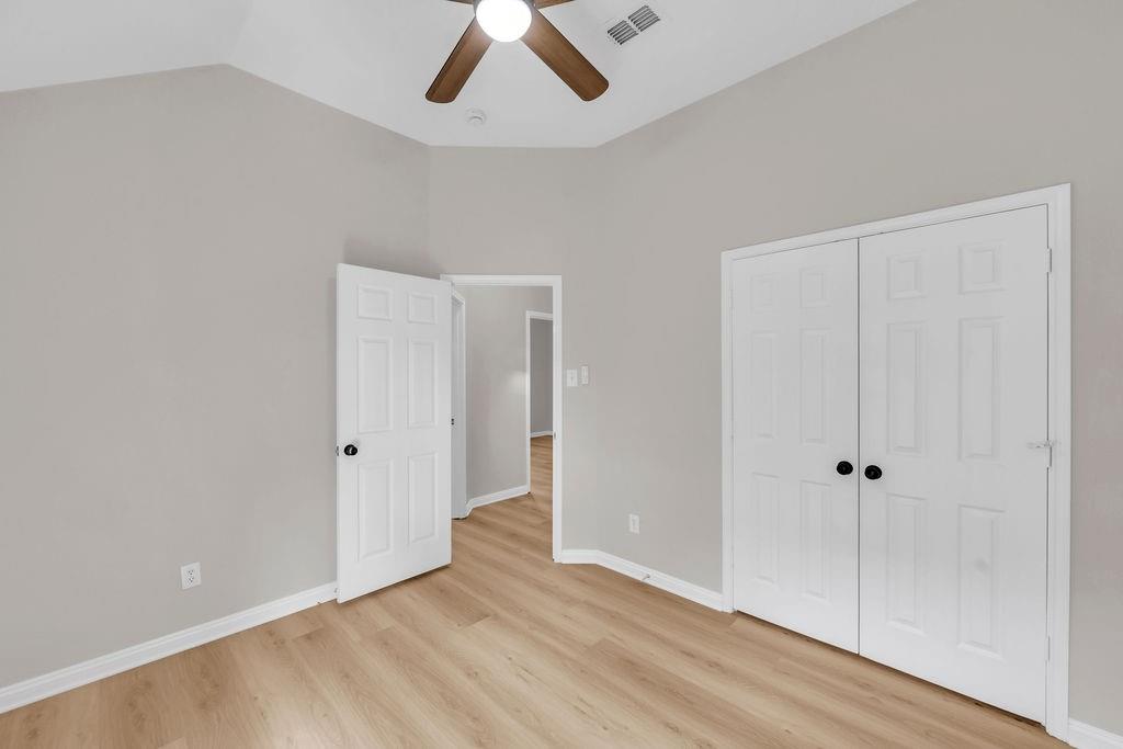 Vaulted ceiling with a central paddle fan, wood-finish flooring, and double-door closet cabinetry