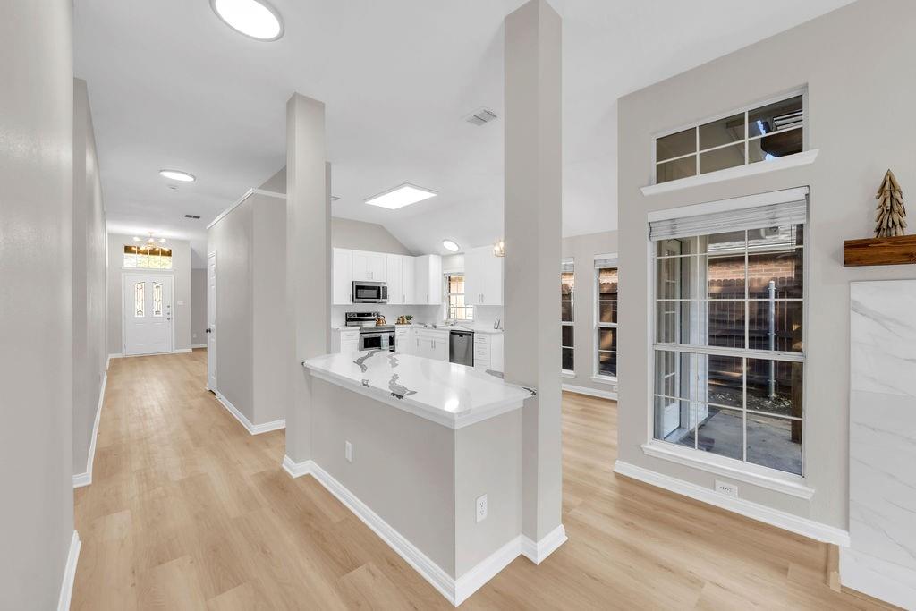 Open concept interior featuring light-toned wood-finish flooring, a kitchen island with a stone-surfaced countertop, vaulted ceilings, and large windows with transom panels