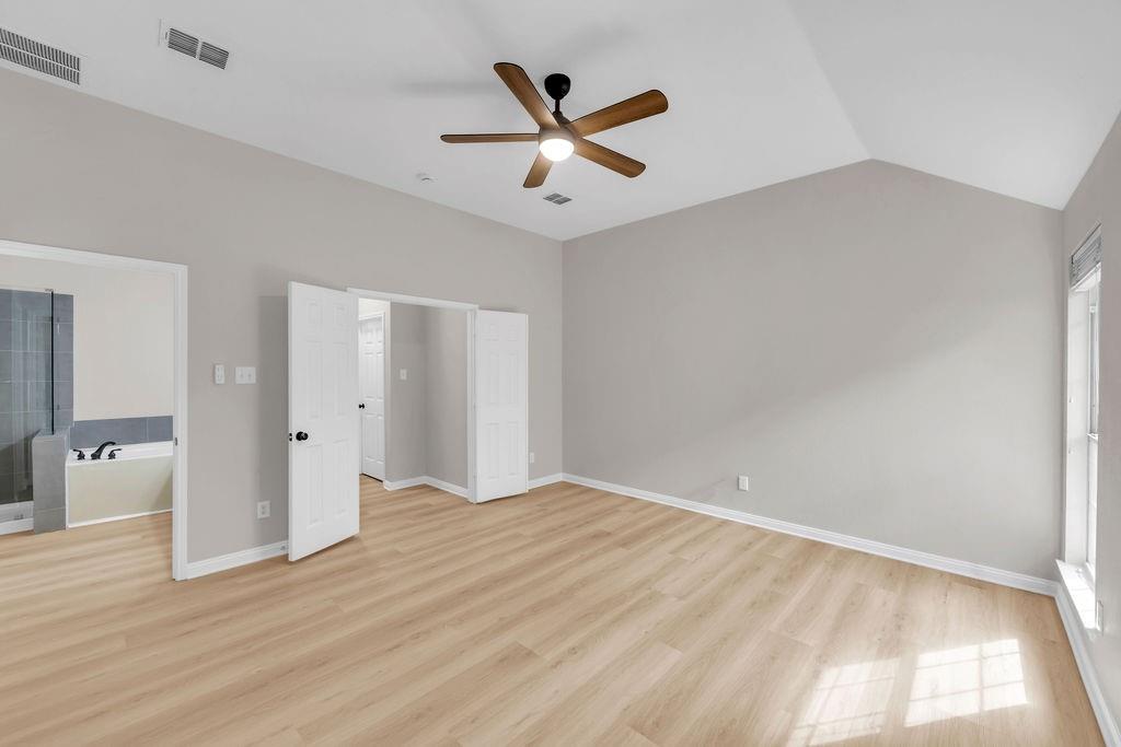 Vaulted ceiling featuring a central five-blade light fixture, neutral wall finishes, wood-finish flooring, and double-door entry
