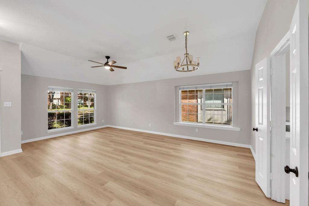 Vaulted ceiling featuring a multi-arm chandelier, wood-finish flooring, and multiple windows with grid detailing