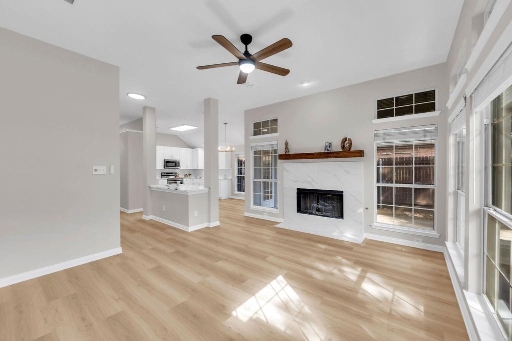 Living area featuring wood-finish flooring, a fireplace with a stone-surround facade and wood mantel, recessed lighting, a ceiling fan, and large windows with transom accents