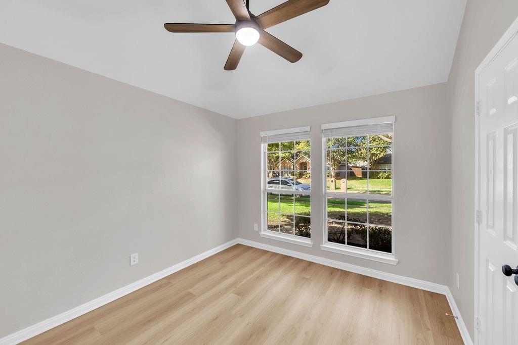 Neutral-toned interior featuring wood-finish flooring, a central ceiling fan with integrated lighting, and dual windows with grid detailing