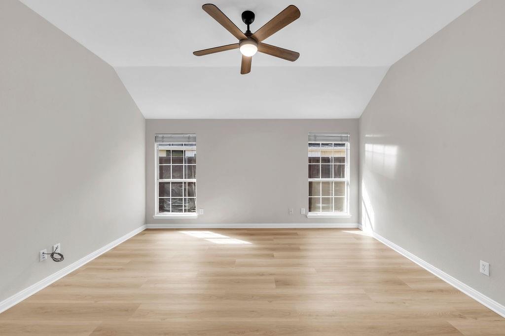 Vaulted ceiling with a central multi-blade ceiling fan, wood-finish flooring, and dual windows with grid mullions