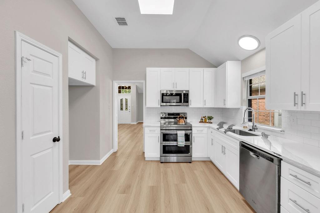 Kitchen featuring white Shaker-style cabinetry, stainless steel appliances, white subway tile backsplash, solid-surface countertops, and wood-finish flooring