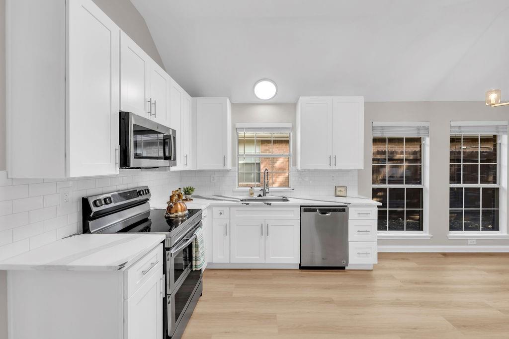 Kitchen featuring white shaker cabinetry, stainless steel appliances, subway tile backsplash, light wood-finish flooring, and vaulted ceilings