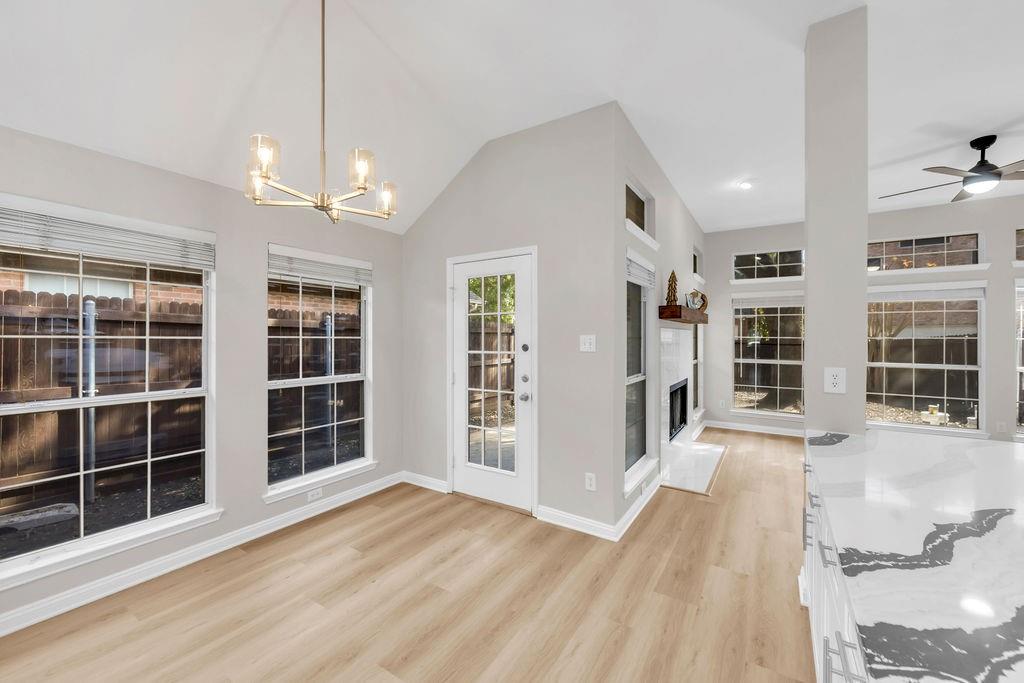 Vaulted ceiling featuring a modern metal chandelier, wood-finish flooring, floor-to-ceiling windows, and a built-in fireplace with a stone surround and timber mantel