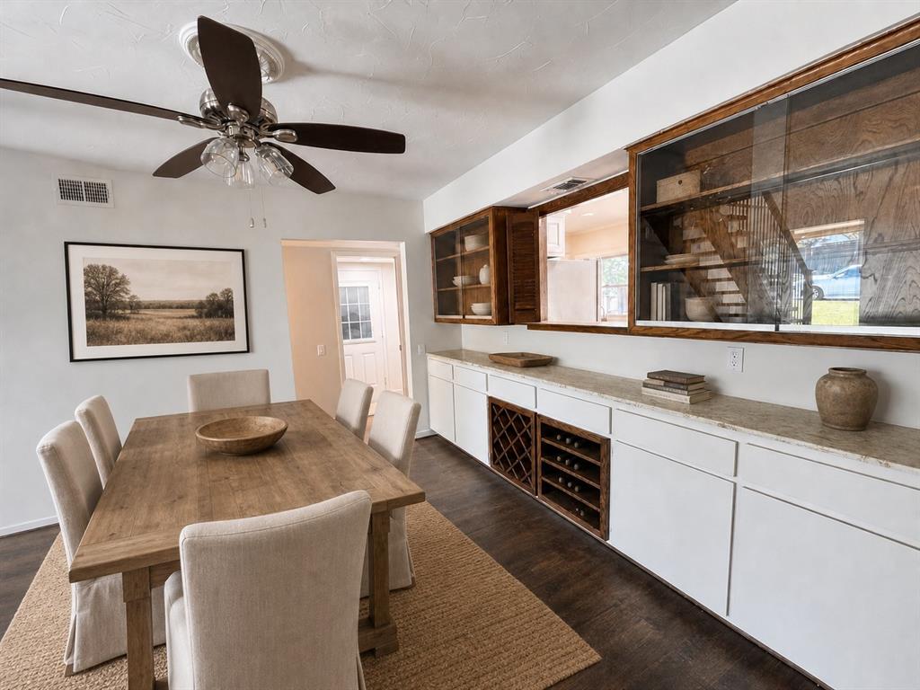 Custom built-in cabinetry featuring glass-front display sections, stone countertop, dedicated wine storage, wood-finish flooring, and a multi-blade ceiling fan with integrated lighting