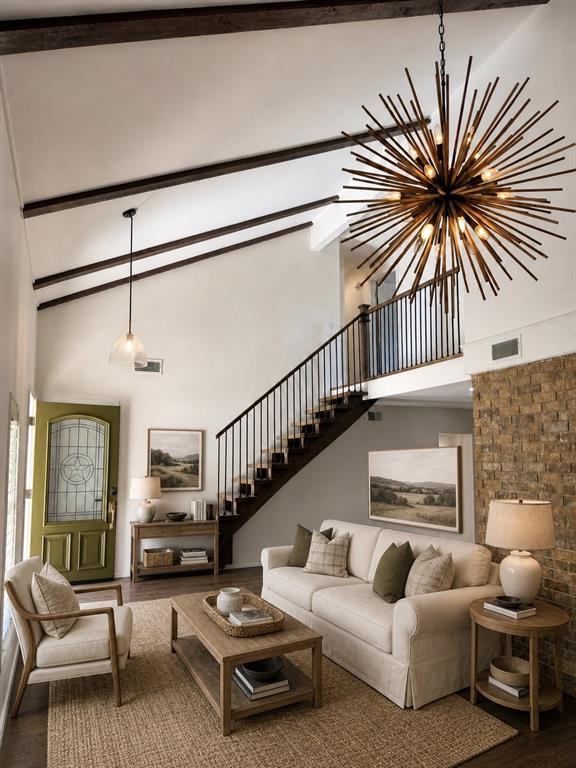 Vaulted ceilings with exposed beams, starburst chandelier, staircase featuring metal balusters, and floor-to-ceiling textured stone accent wall
