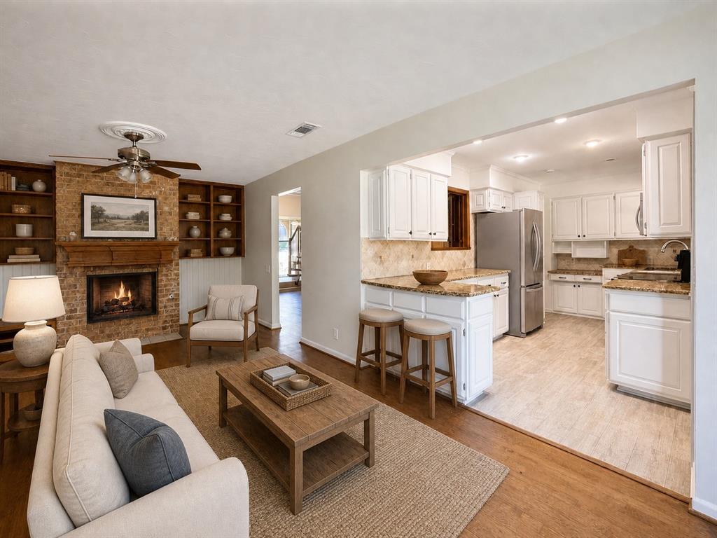 Living area featuring a floor-to-ceiling brick fireplace with wood mantel, built-in shelving, wood-finish flooring, white cabinetry, and stone countertops