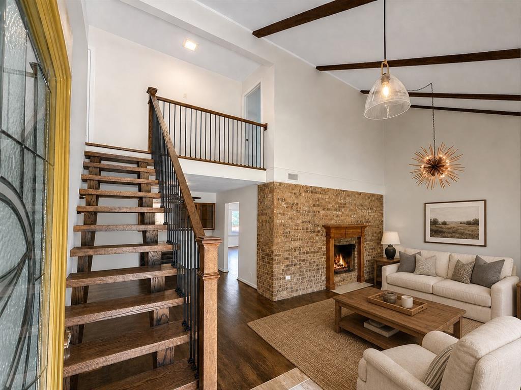 Exposed wood ceiling beams, brick fireplace surround, open-tread staircase with metal balusters, and vaulted ceilings