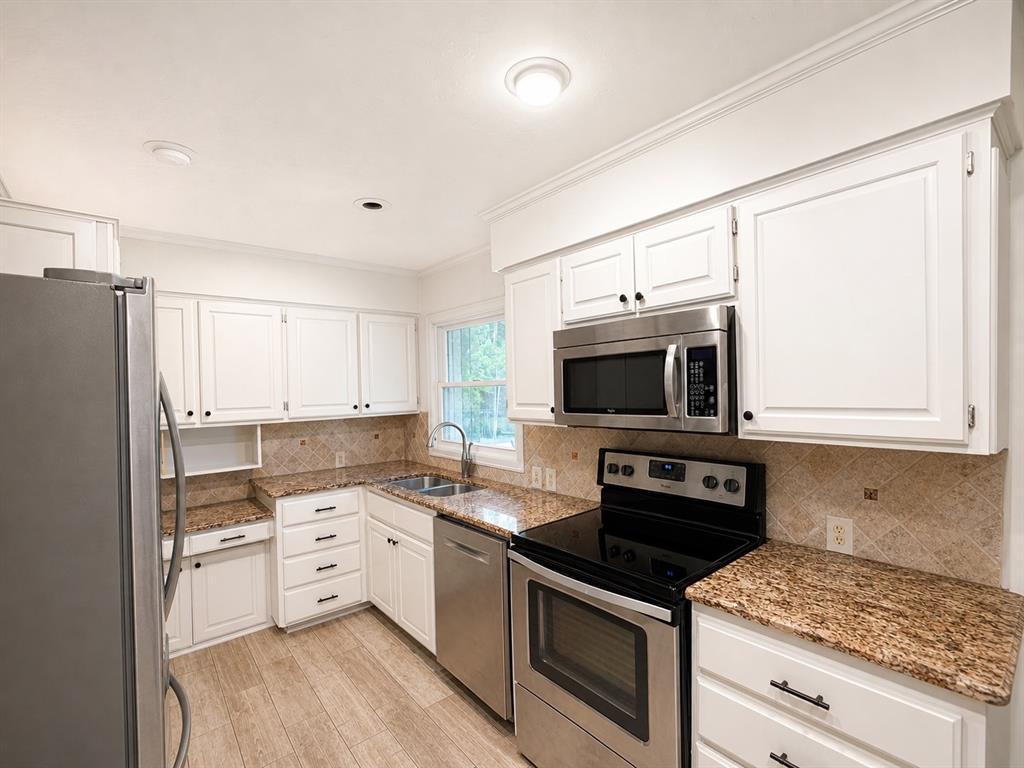 Kitchen featuring white cabinetry, stone-surface countertops, stone tile backsplash, stainless steel appliances, and wood-finish flooring