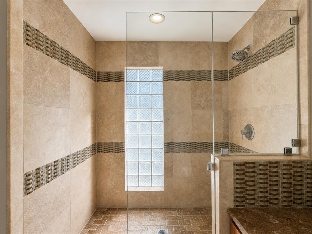Walk-in shower featuring natural stone wall tile, decorative mosaic tile accents, a glass block privacy window, frameless glass enclosure, and a wall-mounted showerhead