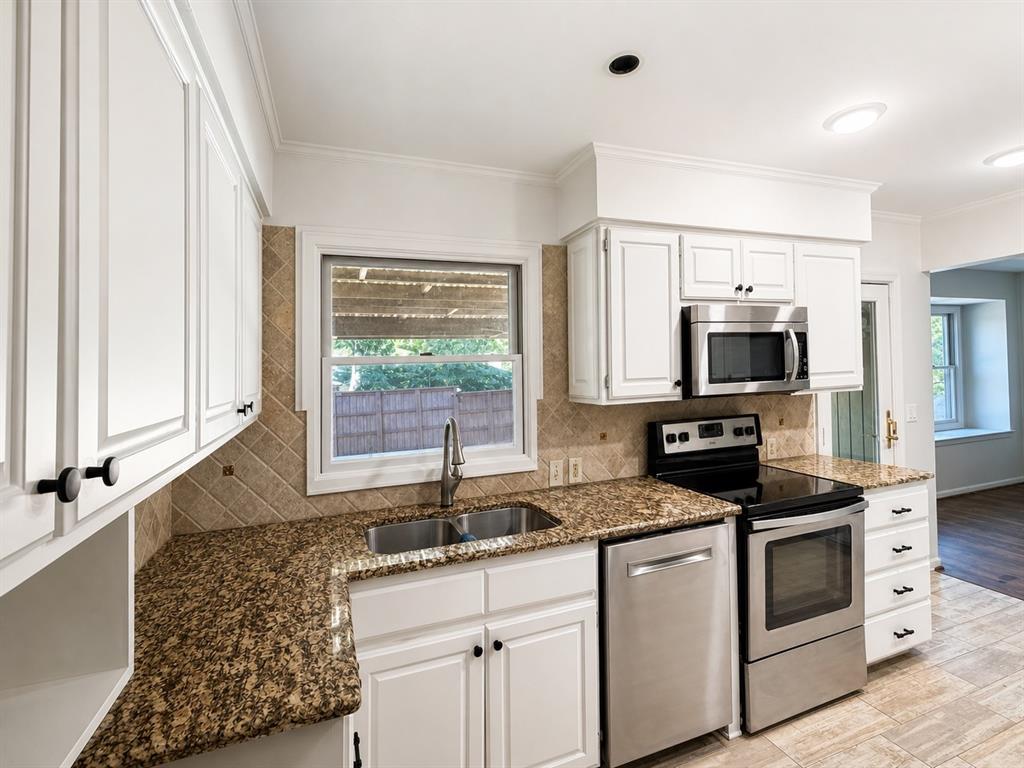 Kitchen featuring white cabinetry, stone-surface countertops, tile backsplash, stainless steel appliances, and a double-basin undermount sink
