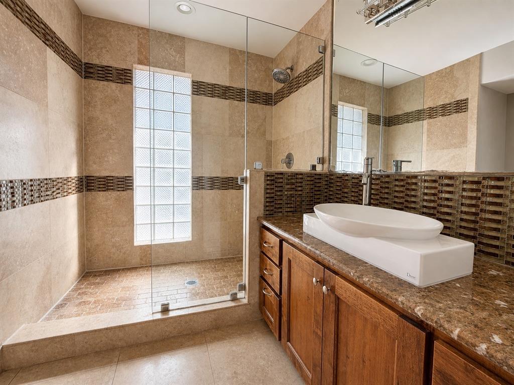 Walk-in shower featuring glass paneling, glass block window, and horizontal accent tile, paired with a wood vanity, stone-finish countertop, and vessel sink