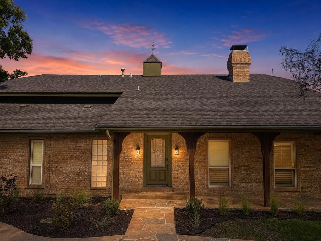 Brick exterior featuring a covered entryway with wood-post supports, a stone-paved walkway, a masonry chimney, and a decorative cupola Brick exterior featuring a covered entryway with wood-post supports, a stone-paved walkway, a masonry chimney, and a decorative cupola
