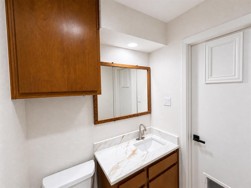 Bathroom featuring a vanity with a stone-finish countertop, undermount sink, brushed nickel faucet, wall-mounted wood-finish cabinetry, and a tri-fold medicine cabinet