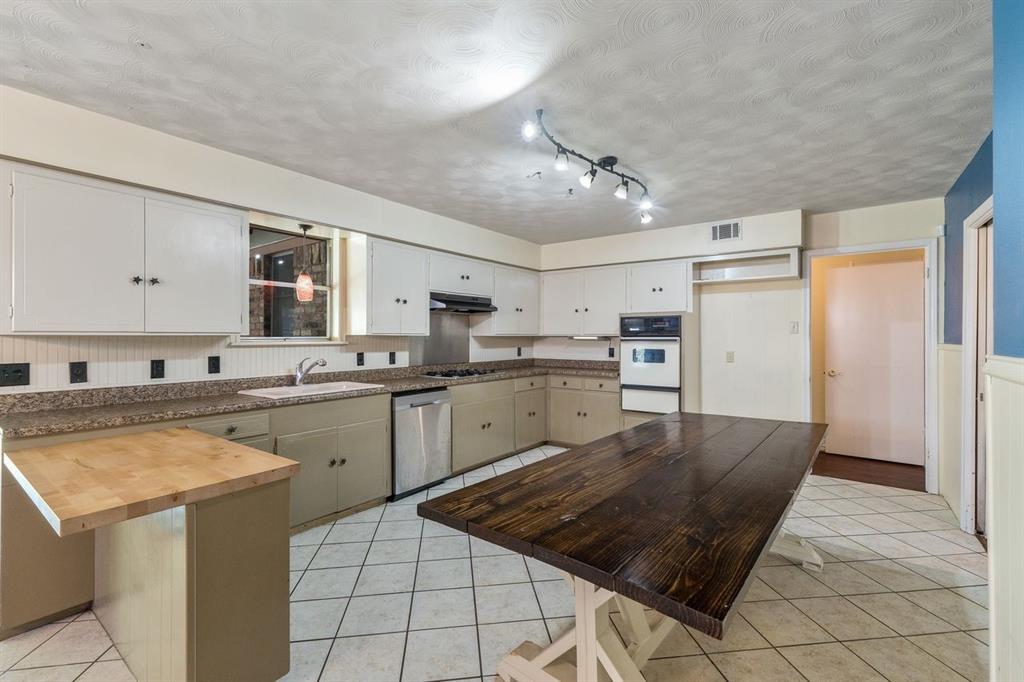 Kitchen featuring white upper cabinetry, multi-toned lower cabinetry, stainless steel dishwasher, built-in wall oven, and ceramic tile flooring