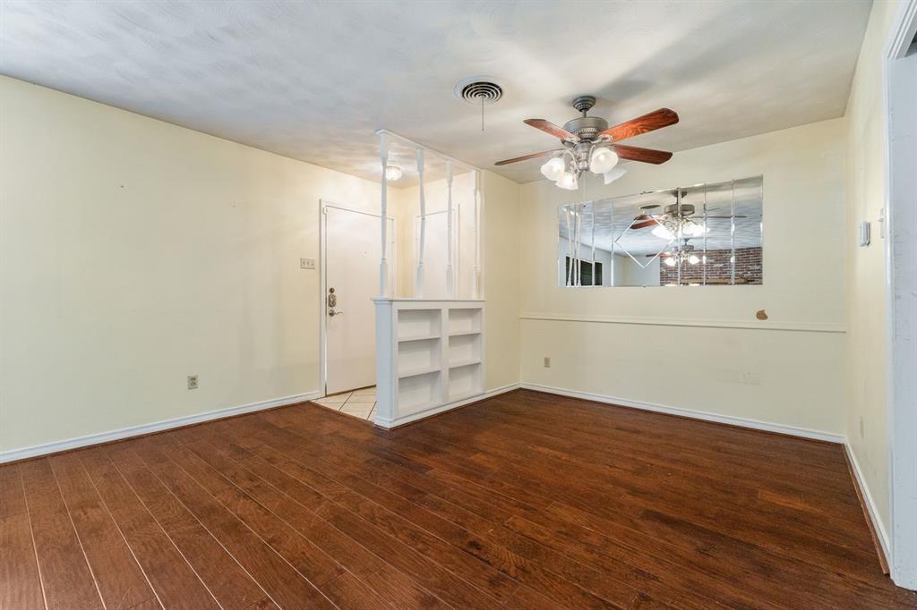 Living area featuring wood-finish flooring, a built-in bookshelf room divider with decorative spindles, a mirrored wall accent, and a ceiling fan with integrated lighting