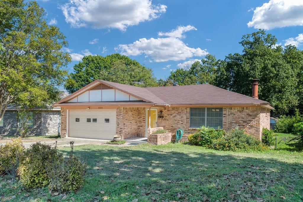 Single-story brick exterior featuring a gable roof, integrated garage, chimney, and stone-accented landscaping