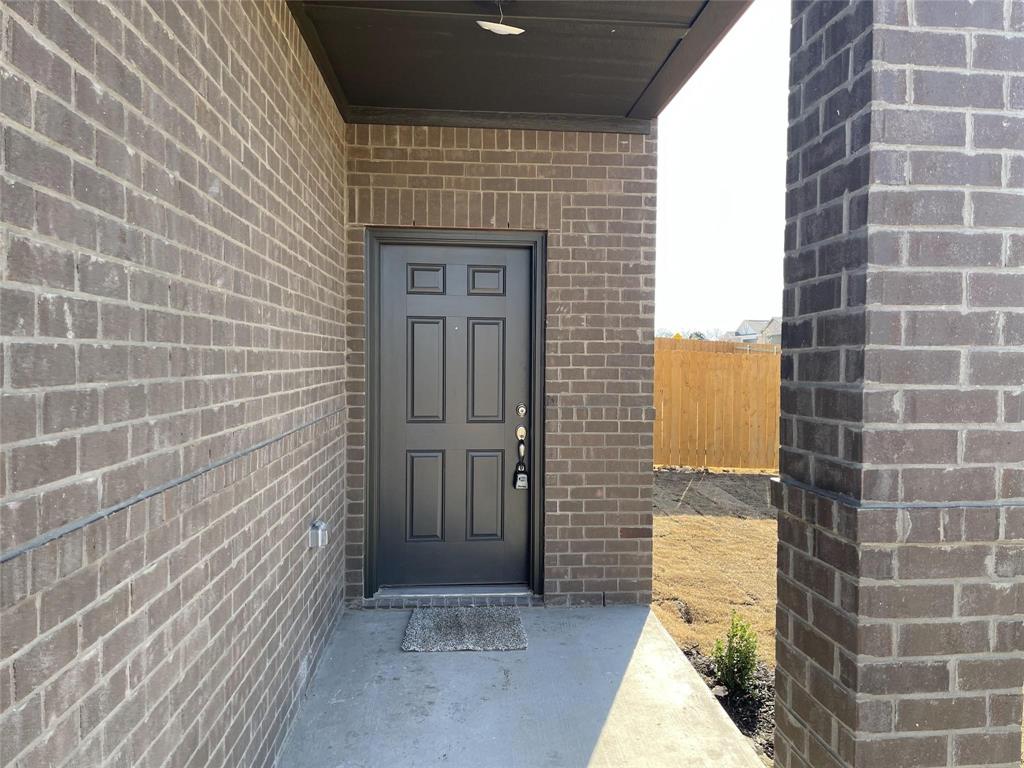 Covered entryway featuring dark brick masonry, a solid six-panel door, and a concrete porch foundation Covered entryway featuring dark brick masonry, a solid six-panel door, and a concrete porch foundation