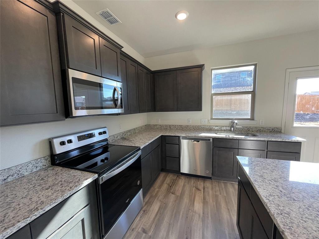 Kitchen featuring dark cabinetry, stone-finish countertops, stainless steel appliances, and wood-finish flooring