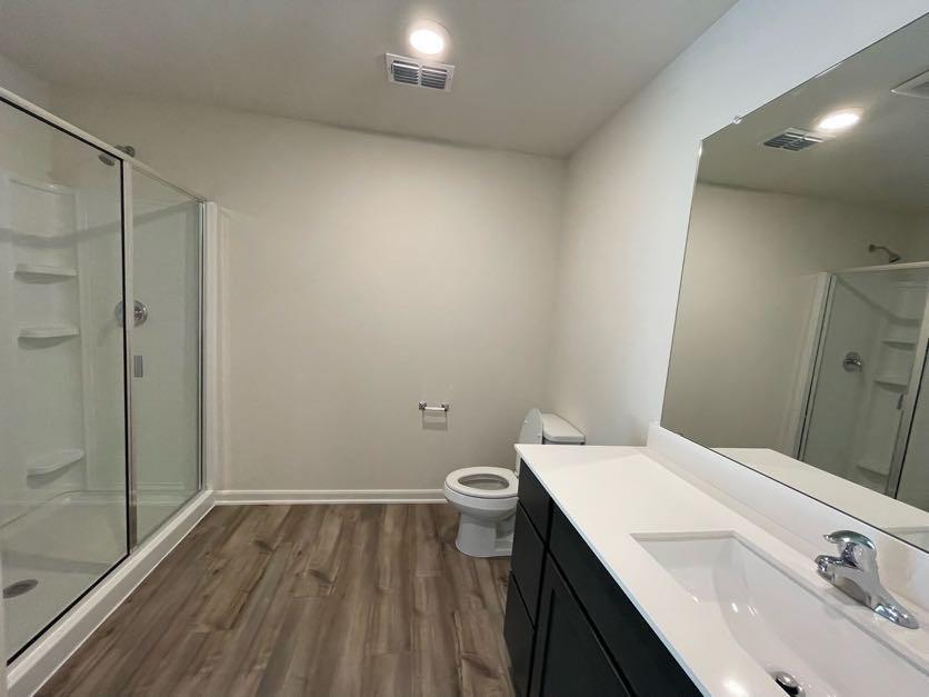 Bathroom featuring a glass-enclosed shower, wood-finish flooring, dark cabinetry with a white countertop, and a full-width wall mirror