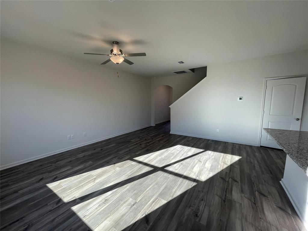 Open-concept interior featuring wood-finish flooring, a ceiling fan with integrated lighting, an arched architectural opening, and a stone-topped peninsula