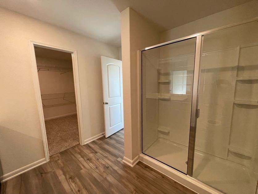Bathroom featuring a glass-enclosed shower stall with integrated shelving, wood-finish flooring, and a walk-in closet with wire shelving