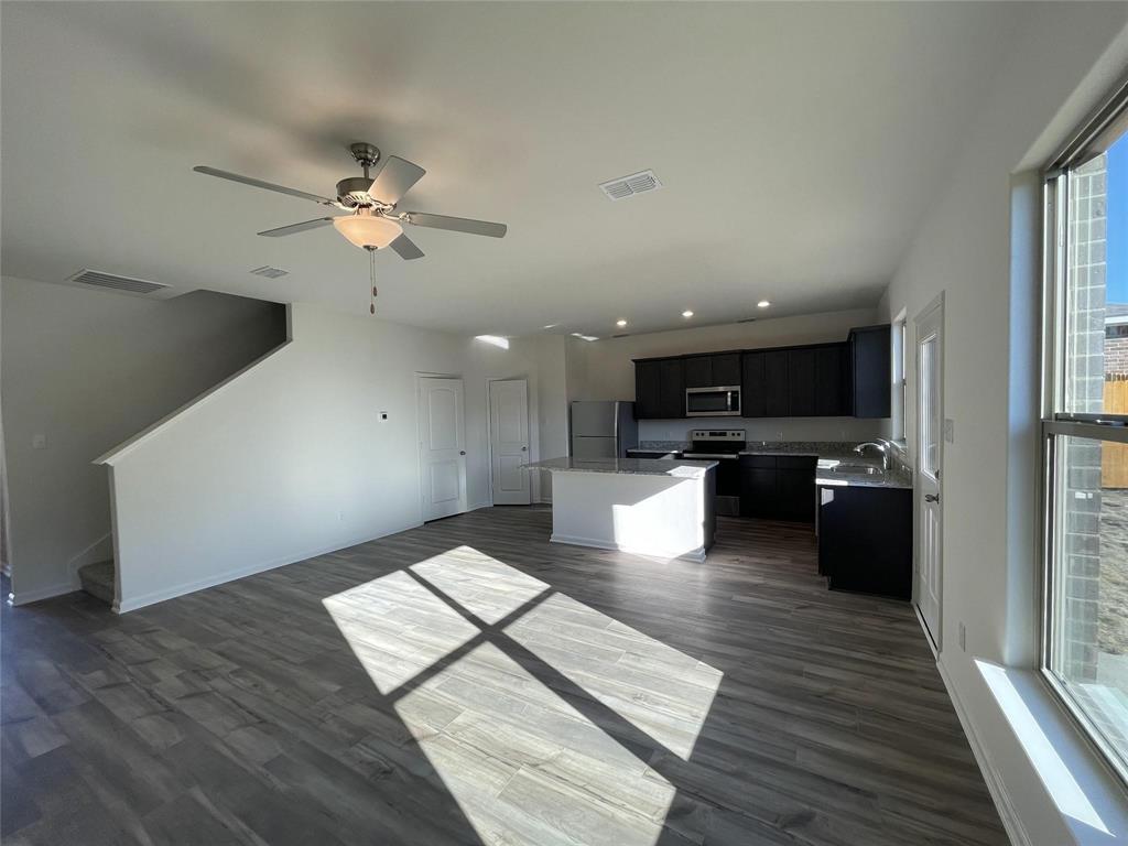 Open-concept floor plan featuring wood-finish flooring, a kitchen with dark cabinetry, a central island with stone-finish countertops, recessed lighting, and a ceiling fan Open-concept floor plan featuring wood-finish flooring, a kitchen with dark cabinetry, a central island with stone-finish countertops, recessed lighting, and a ceiling fan