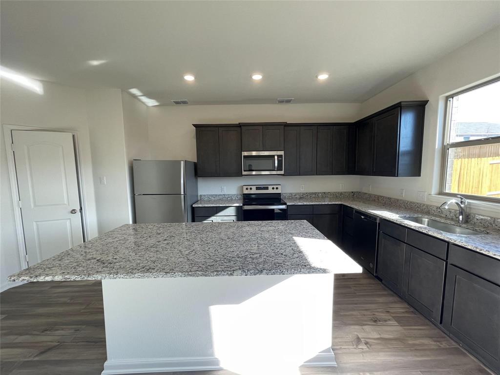 Kitchen featuring dark cabinetry, stone-surface countertops, center island, stainless steel appliances, and wood-finish flooring Kitchen featuring dark cabinetry, stone-surface countertops, center island, stainless steel appliances, and wood-finish flooring