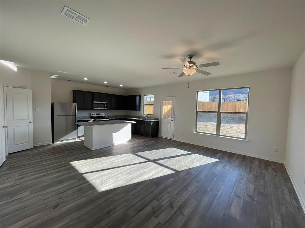 Open-concept kitchen featuring dark cabinetry, a central island, stainless steel appliances, wood-finish flooring, and a ceiling fan Open-concept kitchen featuring dark cabinetry, a central island, stainless steel appliances, wood-finish flooring, and a ceiling fan