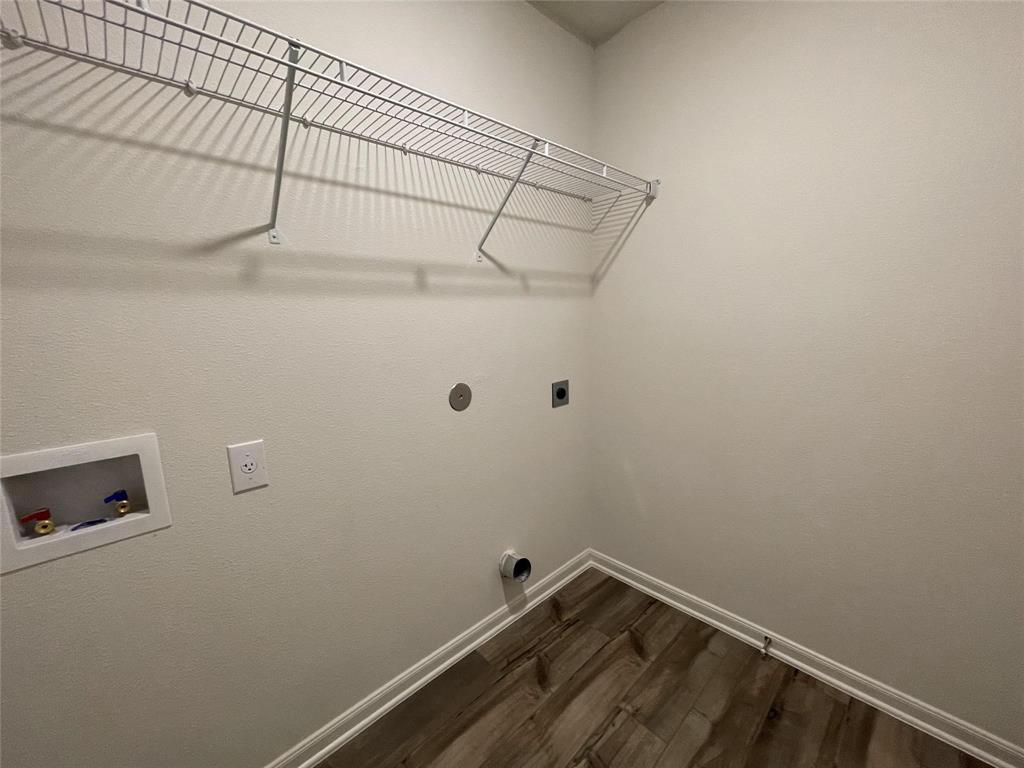 Utility space featuring wood-finish flooring, a wall-mounted wire shelving system, and dedicated water and electrical hookups
