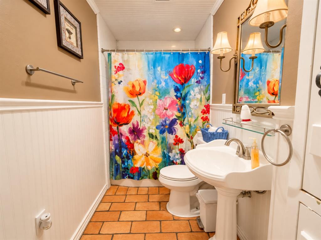 Bathroom featuring white beadboard wainscoting, terra-cotta tile flooring, a pedestal sink with a metallic faucet, and a beadboard ceiling