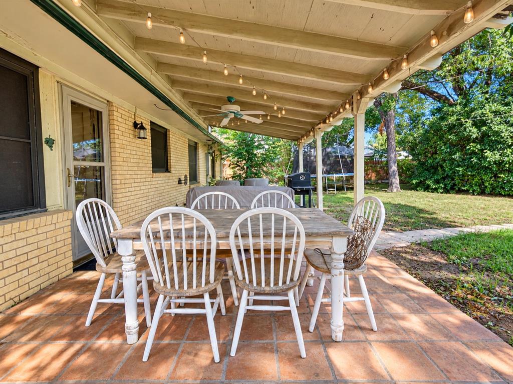 Covered patio featuring a yellow brick exterior wall, terracotta-style flooring, a wooden ceiling structure with an integrated ceiling fan, and string lighting