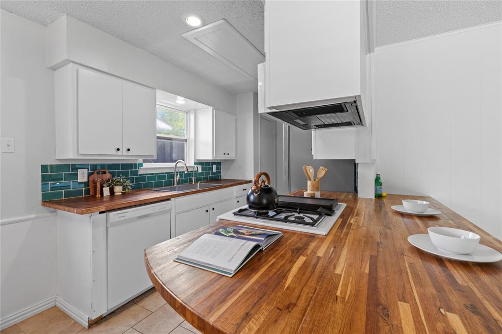 Kitchen featuring wood-surface countertops, blue subway tile backsplash, integrated gas cooktop, white cabinetry, and a stainless steel sink