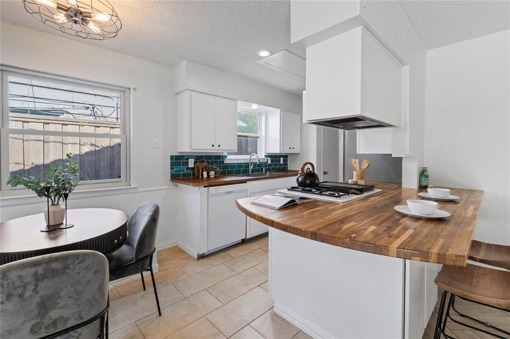 Kitchen featuring wood-finish countertops, white cabinetry, dark blue tile backsplash, gas cooktop, and tile flooring